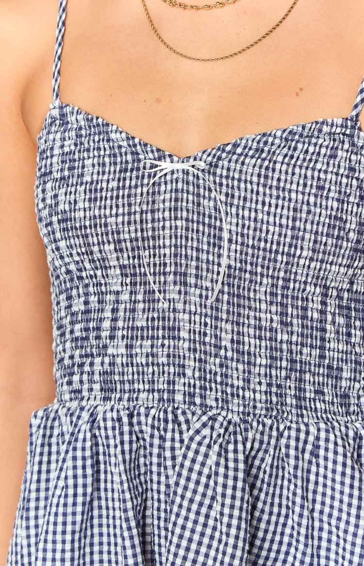 Close-up of the navy gingham playsuit showing the shirred bodice, sweetheart neckline, and small white bow detail