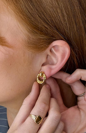 A close-up side profile of a model wearing the Hollie Gold Chunky Hoop Earring, showing its size and polished finish on the ear.