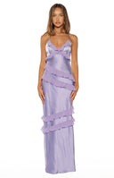A full-length studio shot of our model wearing a light lavender satin maxi dress. This maxi dress features thin spaghetti straps a V-neckline with small ruffle trim and several diagonal tiers of sheer purple ruffles flowing down the length of the skirt.