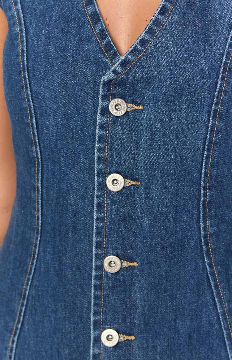 Close-up of the silver buttons and buttonholes on the front placket of a dark wash denim mini dress with orange contrast stitching