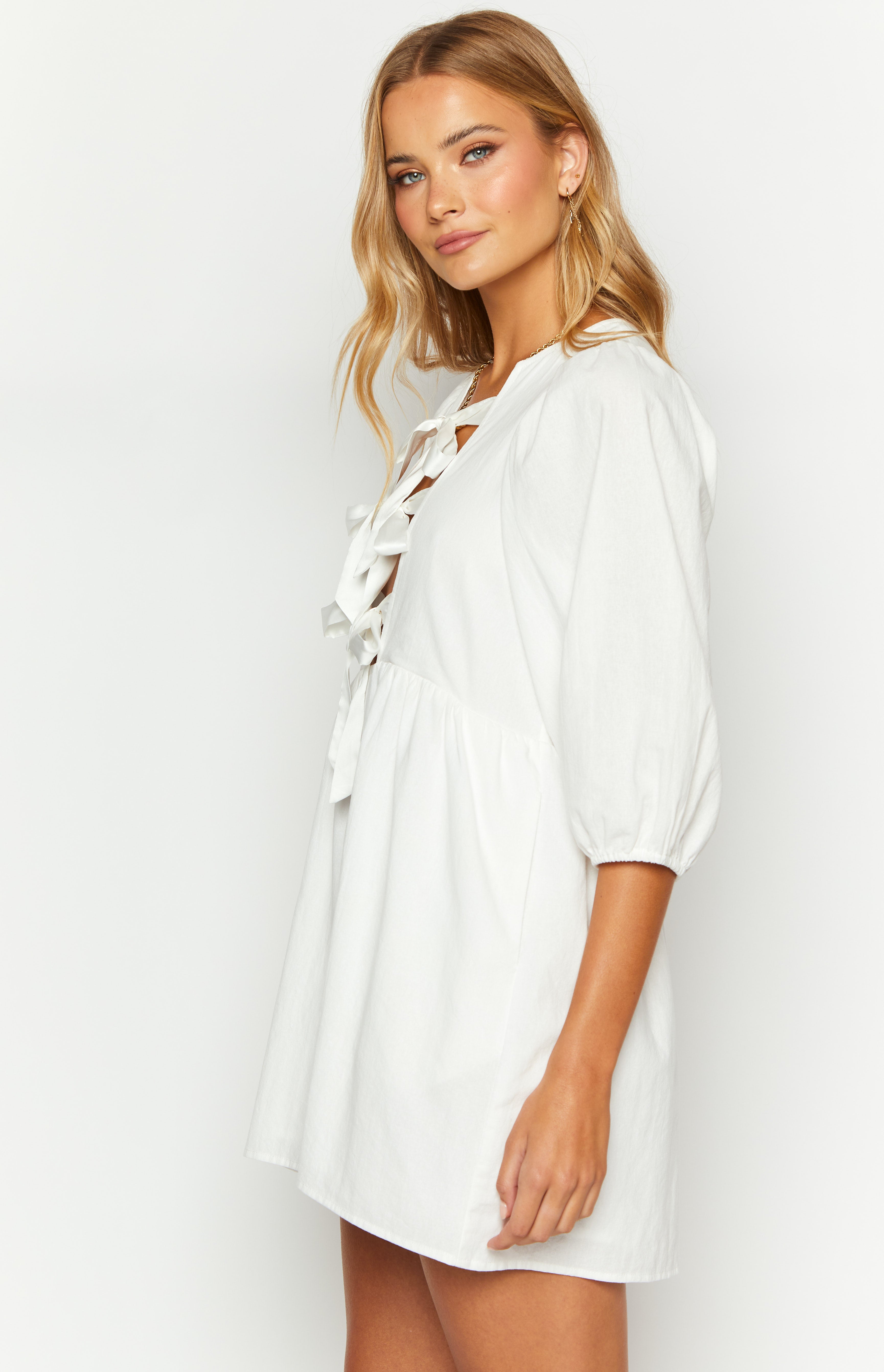 Side view of a white mini dress featuring a lace-up V-neckline with ties and 3/4 length puff sleeves with elasticated cuffs