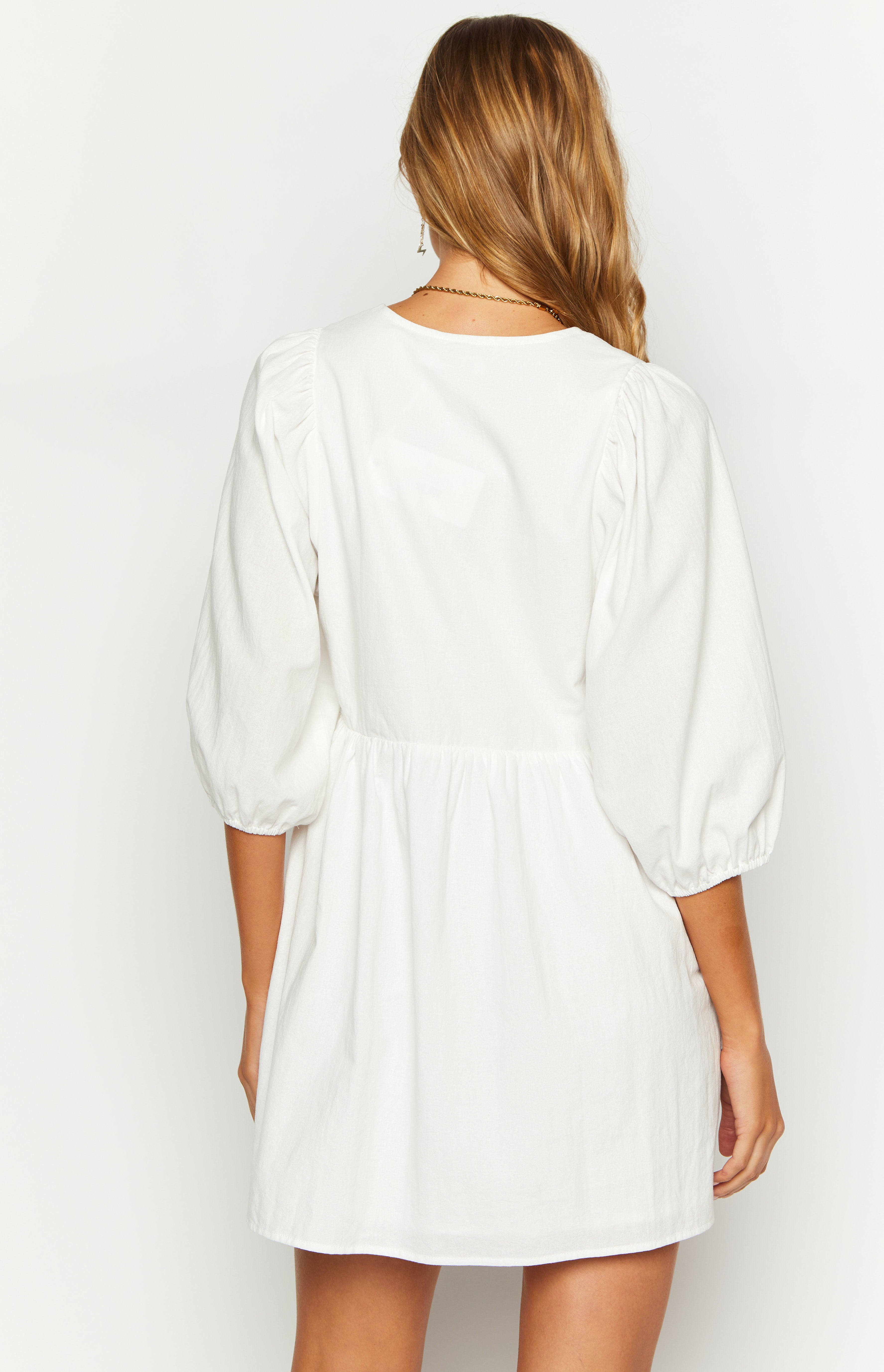 Rear view of a white mini dress with a round neck, puffed 3/4 sleeves, and a gathered waist