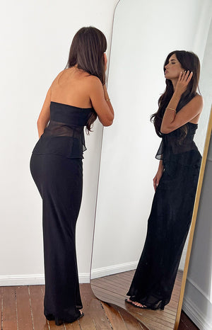 Side view of a black fitted maxi skirt with a smooth, flowing fabric and floor-length hem
