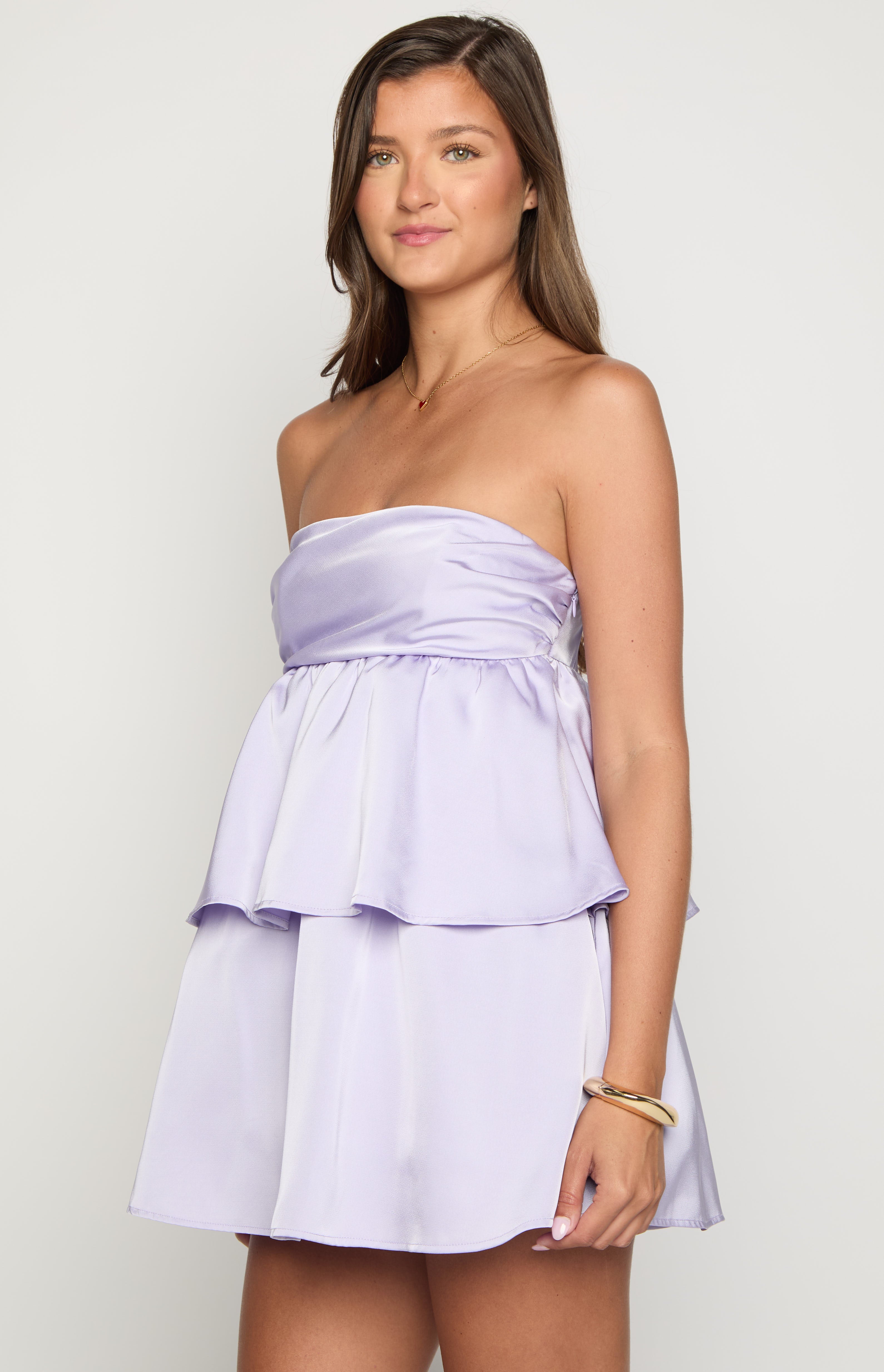 Side view of a lilac satin strapless mini dress with tiered ruffle detailing on the skirt