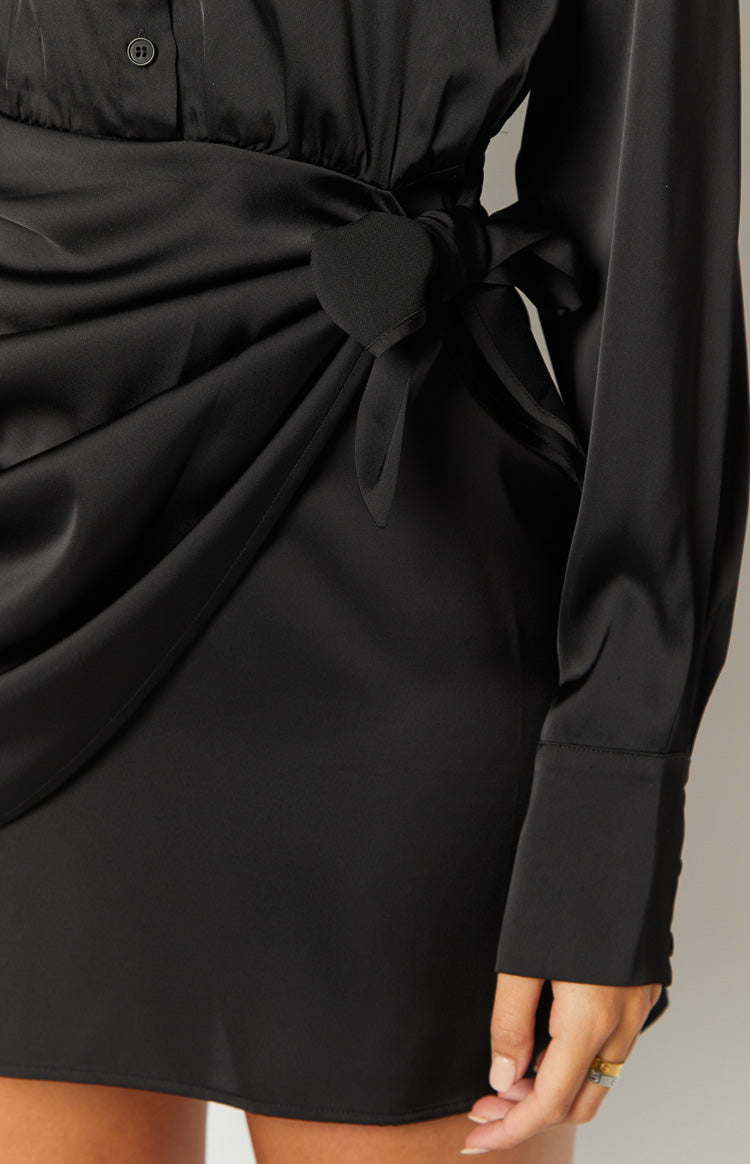Close-up of the tie-front detail on a black mini wrap dress, showing the draped skirt and cuffed long sleeve