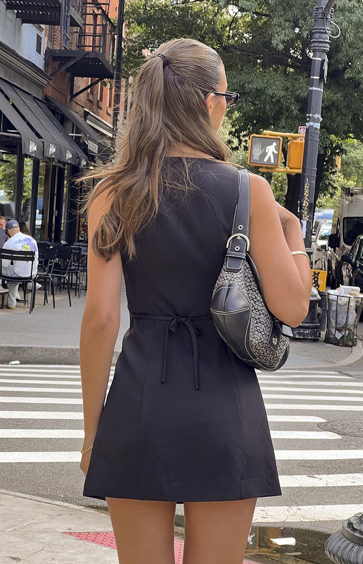 Rear view of a black sleeveless mini dress with a tie-back waist detail and A-line skirt