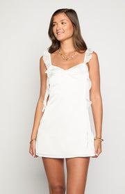Front view of a white satin mini dress with ruffled shoulder straps and side ruffles
