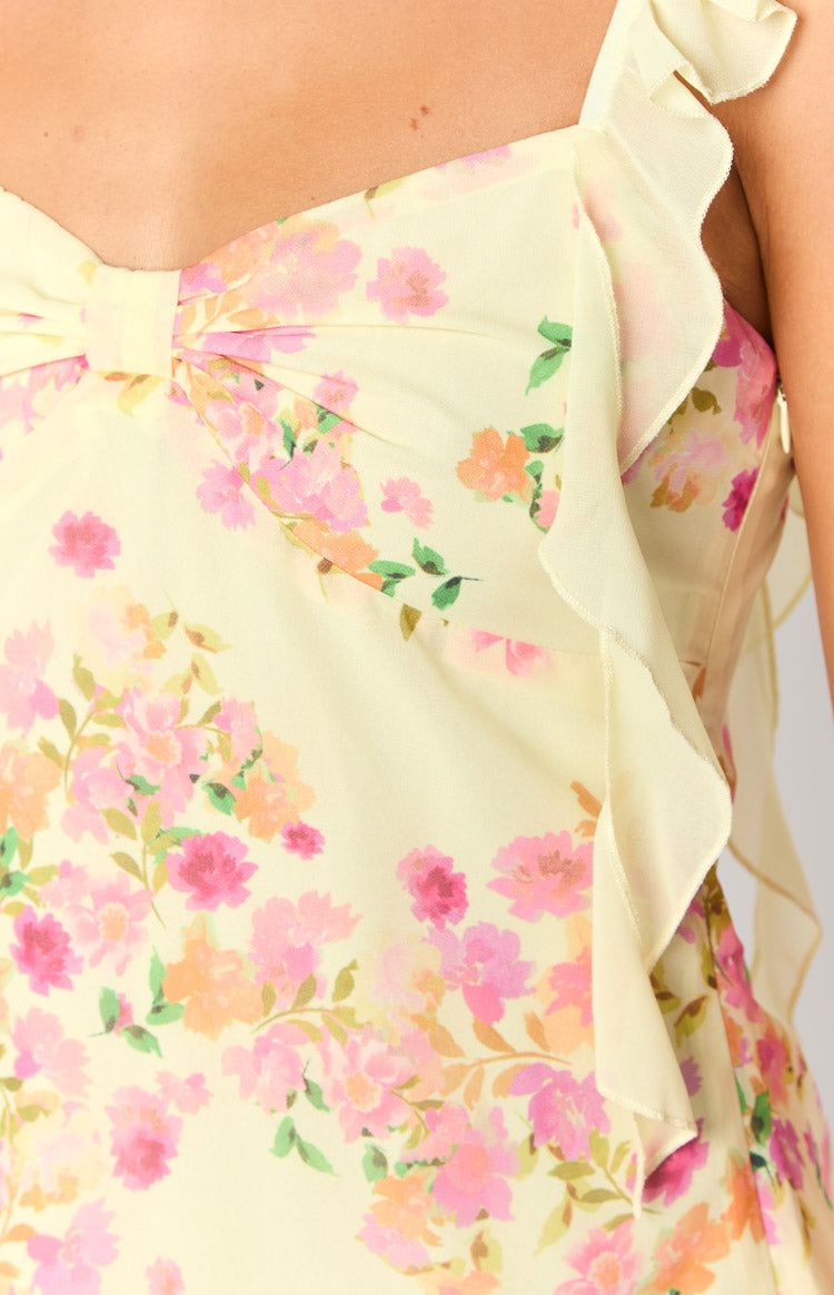 Close-up of the yellow chiffon mini dress showing the pink and orange floral print, bow detail, and ruffled trim