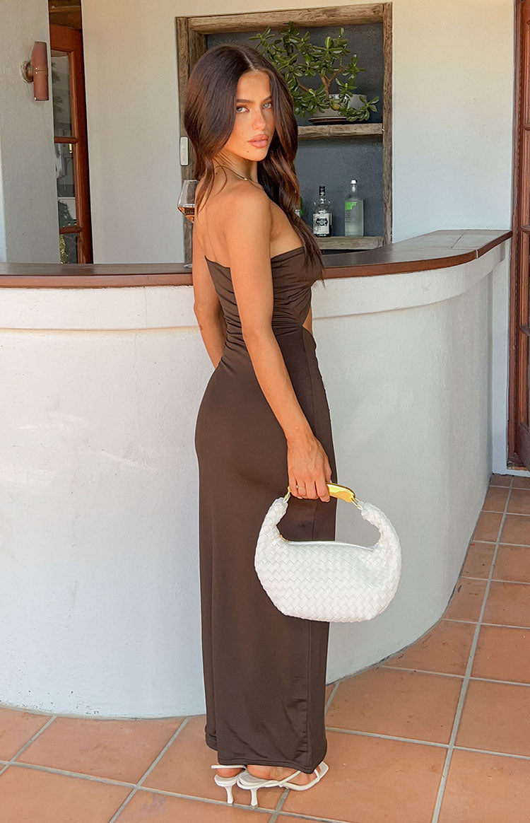 Side view of a brown strapless midi dress with a cutout detail at the waist and a flowing skirt