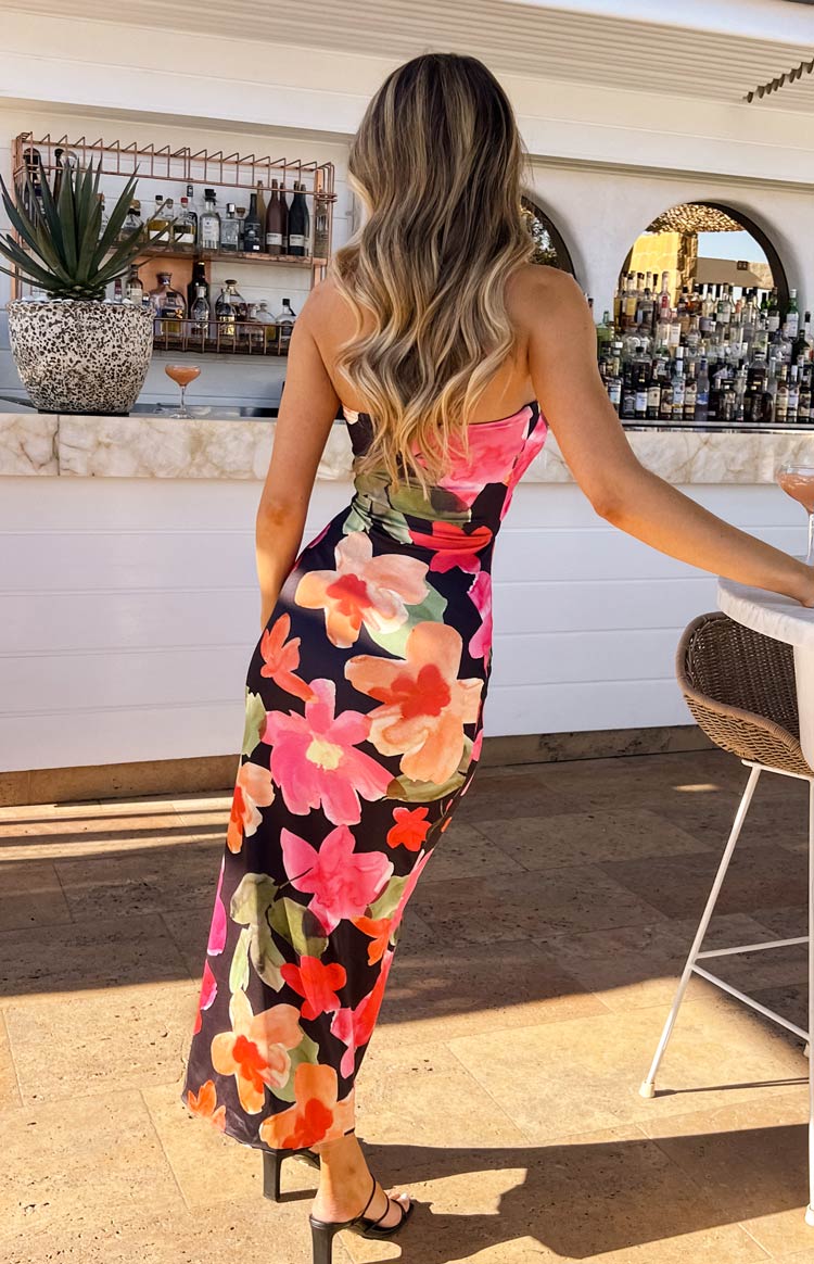 Back view of a black floral strapless midi dress with large pink, orange, and green flowers, showing the fitted silhouette