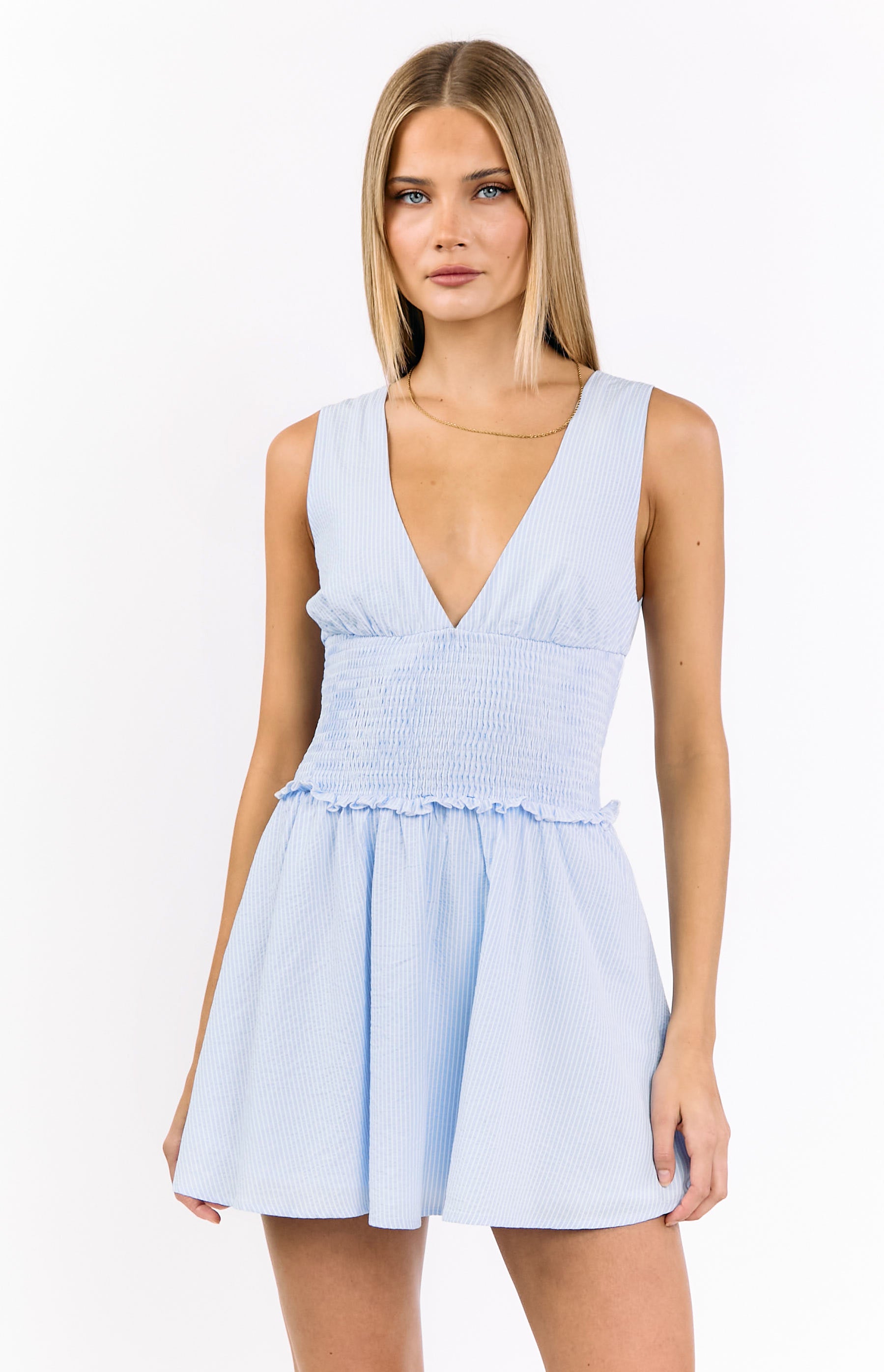 Front view of a light blue stripe mini dress with a deep V-neck, shirred bodice, and ruffled waist
