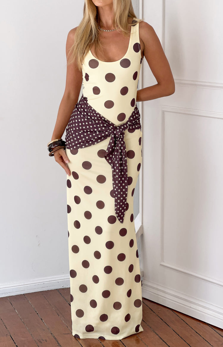 Front view of a yellow maxi dress with large brown polka dots and a brown polka dot scarf tied at the waist