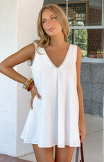 White cotton mini dress with a V-neckline, delicate lace trim, a small bow detail, and vertical textured stripes