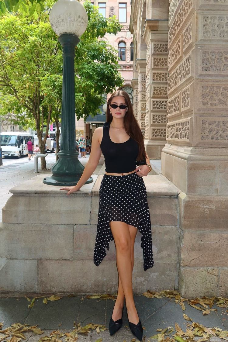 Full view of a black polka dot hanky hem midi skirt with a flowy drape