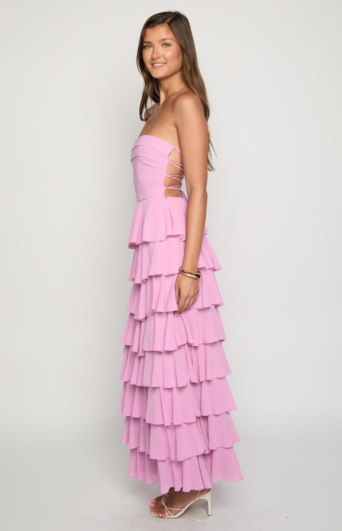 Side view of a pink strapless maxi dress with lace-up side cutouts and tiered ruffles