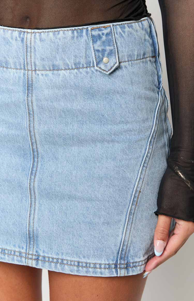 Close-up of light wash denim mini skirt showing a belt loop with silver button, diagonal seam, and contrast stitching