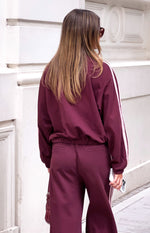 Rear view of a burgundy track jacket with an elasticated hem and pink stripes down the long sleeves