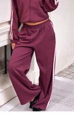 Relaxed fit burgundy track pants featuring a wide leg, elasticated waist, and pink side stripes