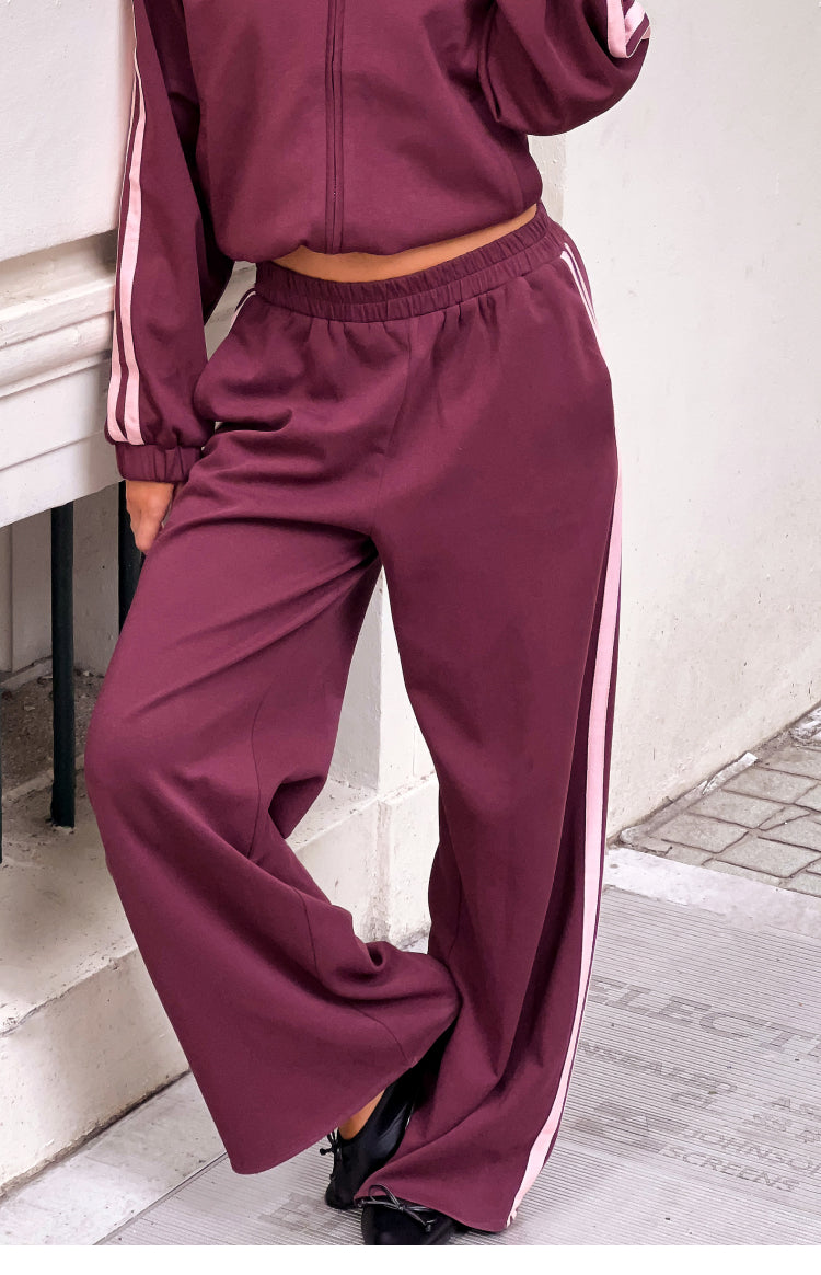 Relaxed fit burgundy track pants featuring a wide leg, elasticated waist, and pink side stripes