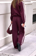 Rear view of burgundy wide-leg track pants with a pink double stripe down each side