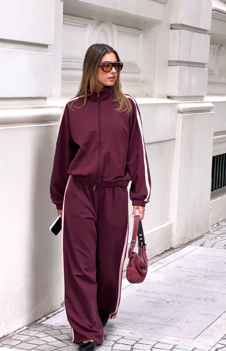 Burgundy wide-leg track pants with full length pink side stripes and a relaxed fit