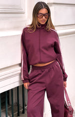 Burgundy track pants with pink side stripes and matching cropped zip-up jacket with high collar