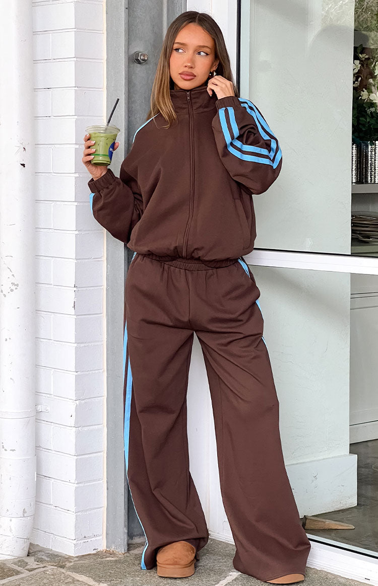 Full length view of chocolate brown track pants with light blue side stripes and a relaxed wide-leg fit