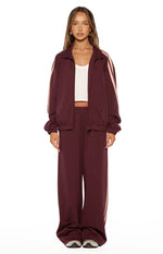 Full length view of burgundy wide-leg track pants with pink side stripes and a relaxed fit