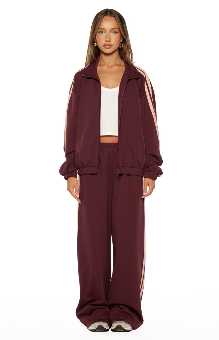 Full length view of burgundy wide-leg track pants with pink side stripes and a relaxed fit