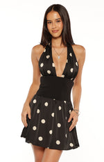 Front view of a black polka dot halter neck mini dress with a deep V-neck and wide black elasticated waistband