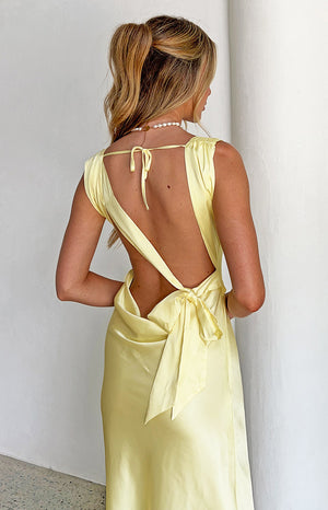 Rear view of a yellow satin maxi dress showing the low open back, thin tie-up straps, and a large bow