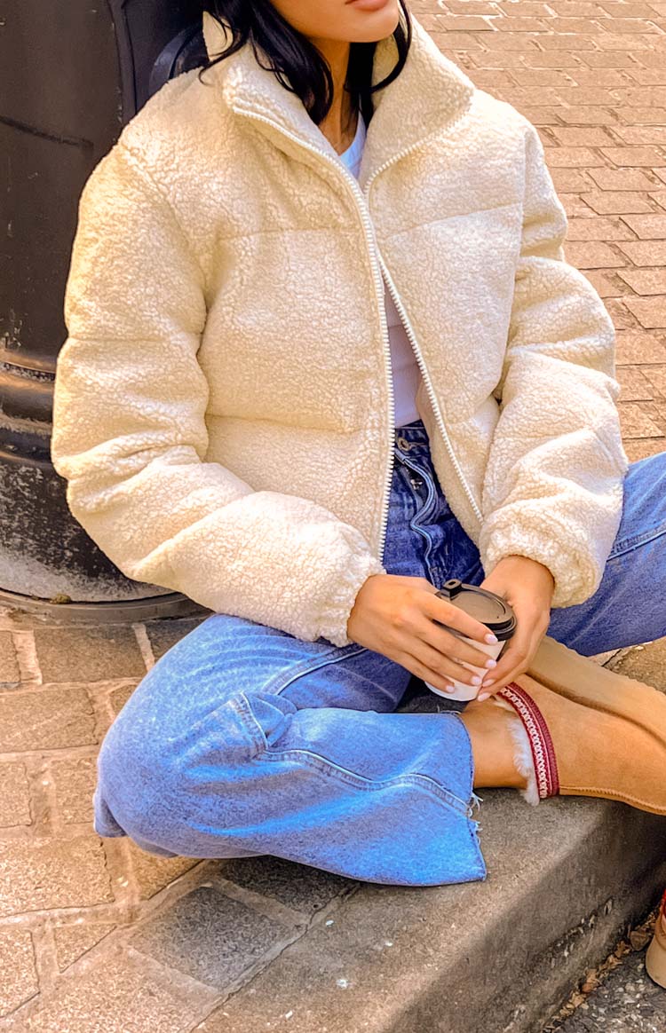 Close-up of the cream teddy puffer jacket's textured fabric, white front zipper, and stand collar