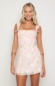 Front view of a pink floral mini dress with a square neckline, ruched bodice, and bow details on the straps