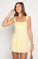 blonde girl wearing a yellow gingham print mini dress with a square neckline and yellow ribbon details