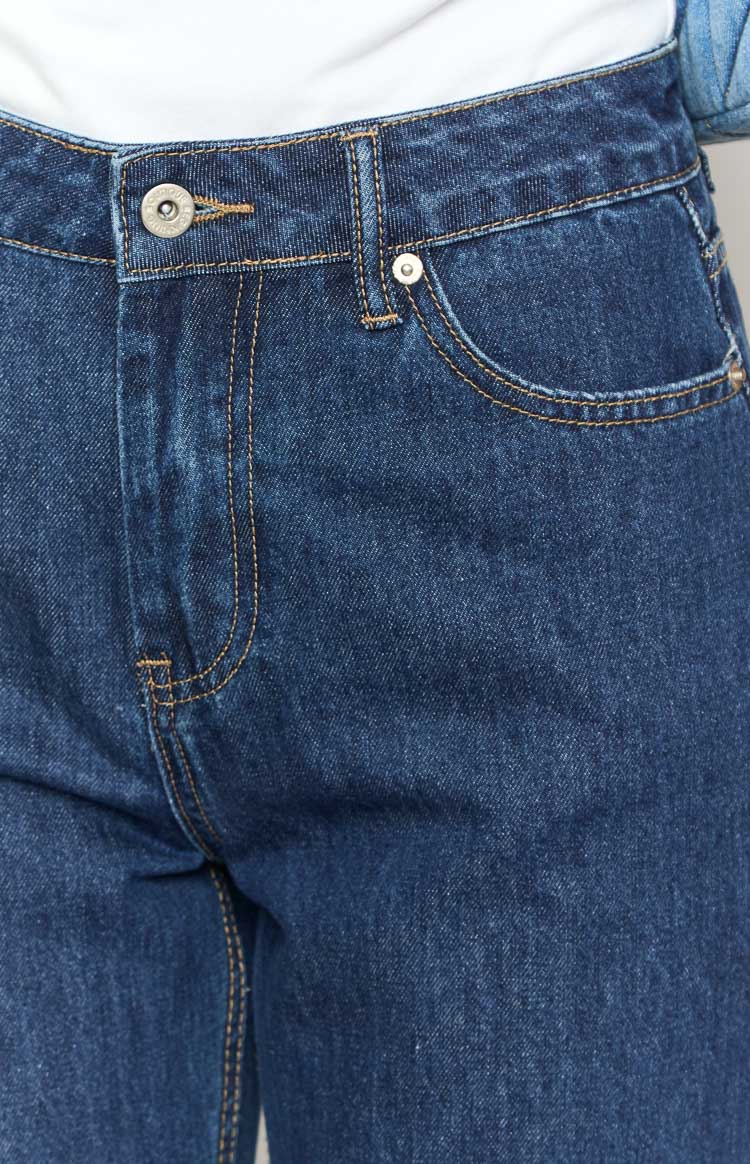 Close-up of the dark blue denim jeans showing the button fly, front pockets, and orange contrast stitching