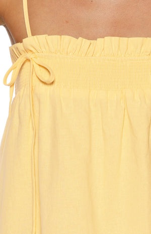 Close-up of the yellow shirred bust detail with a ruffled top edge and decorative tie on a mini dress