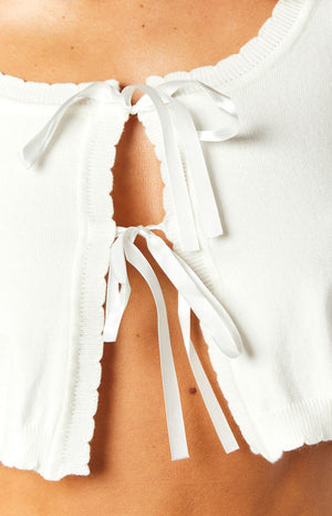 White knit crop top close-up showing the front opening with satin ribbon ties and scalloped edges