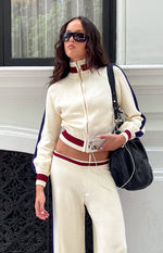 Cropped cream knit zip sweater with high collar, red and white striped cuffs and hem, and navy raglan sleeve stripes