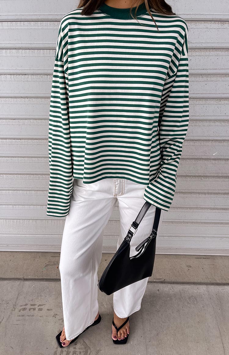 Green and white horizontal striped long-sleeve top with a mock neck, paired with white wide-leg jeans. Black square-toe thong sandals and a black shoulder bag are accessorized