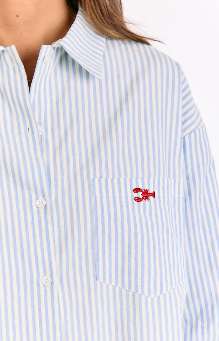 Close-up of the red lobster embroidery on the chest pocket of a blue and white striped button-up shirt