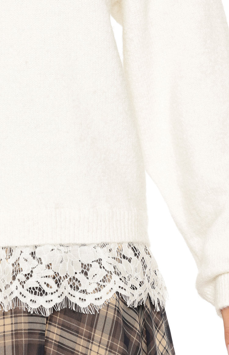 Close-up of the cream knit sweater's hem with a wide white floral lace trim peeking out underneath