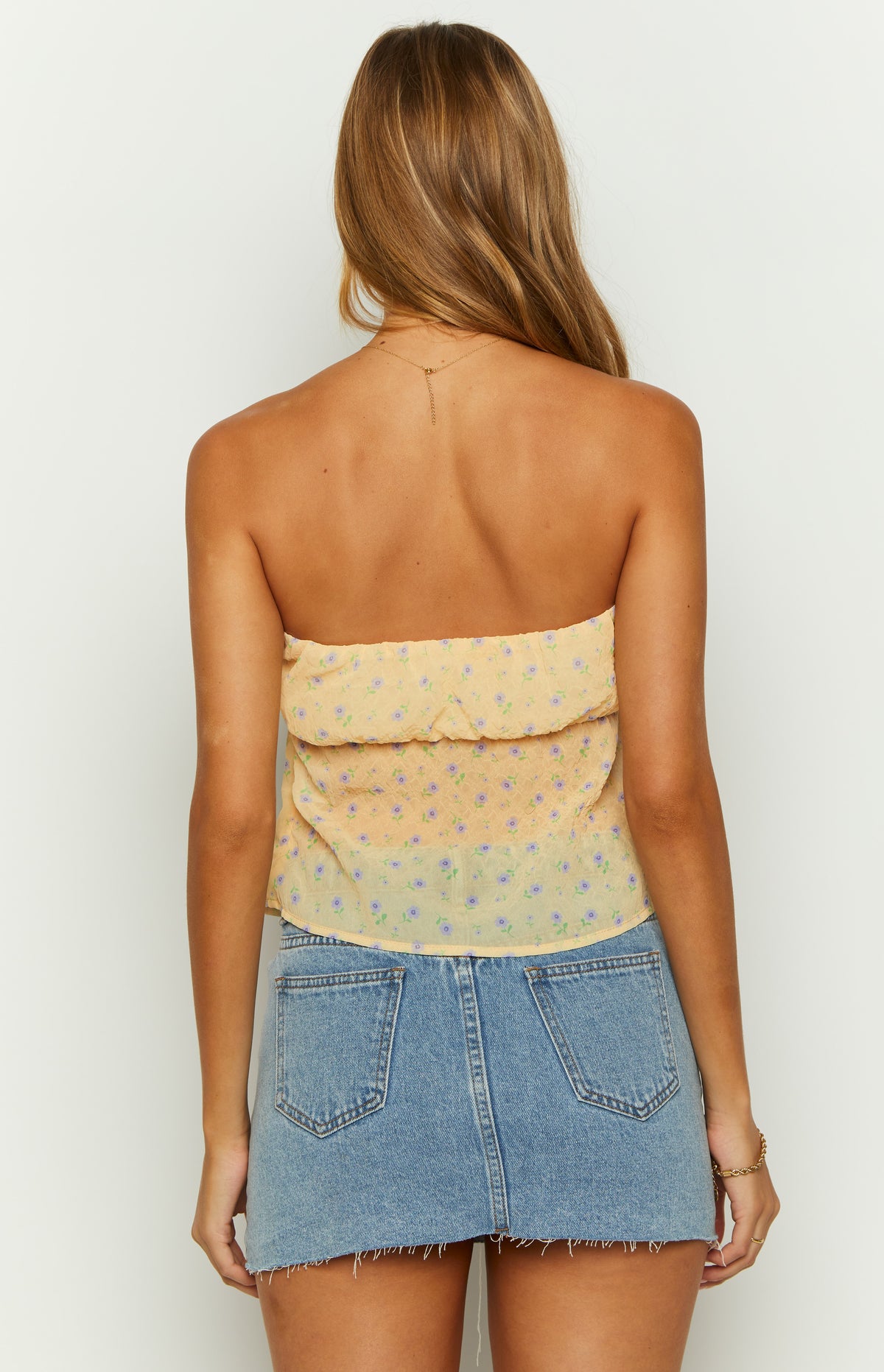 Rear view of the yellow floral strapless top with a gathered ruffled top edge and crinkled texture