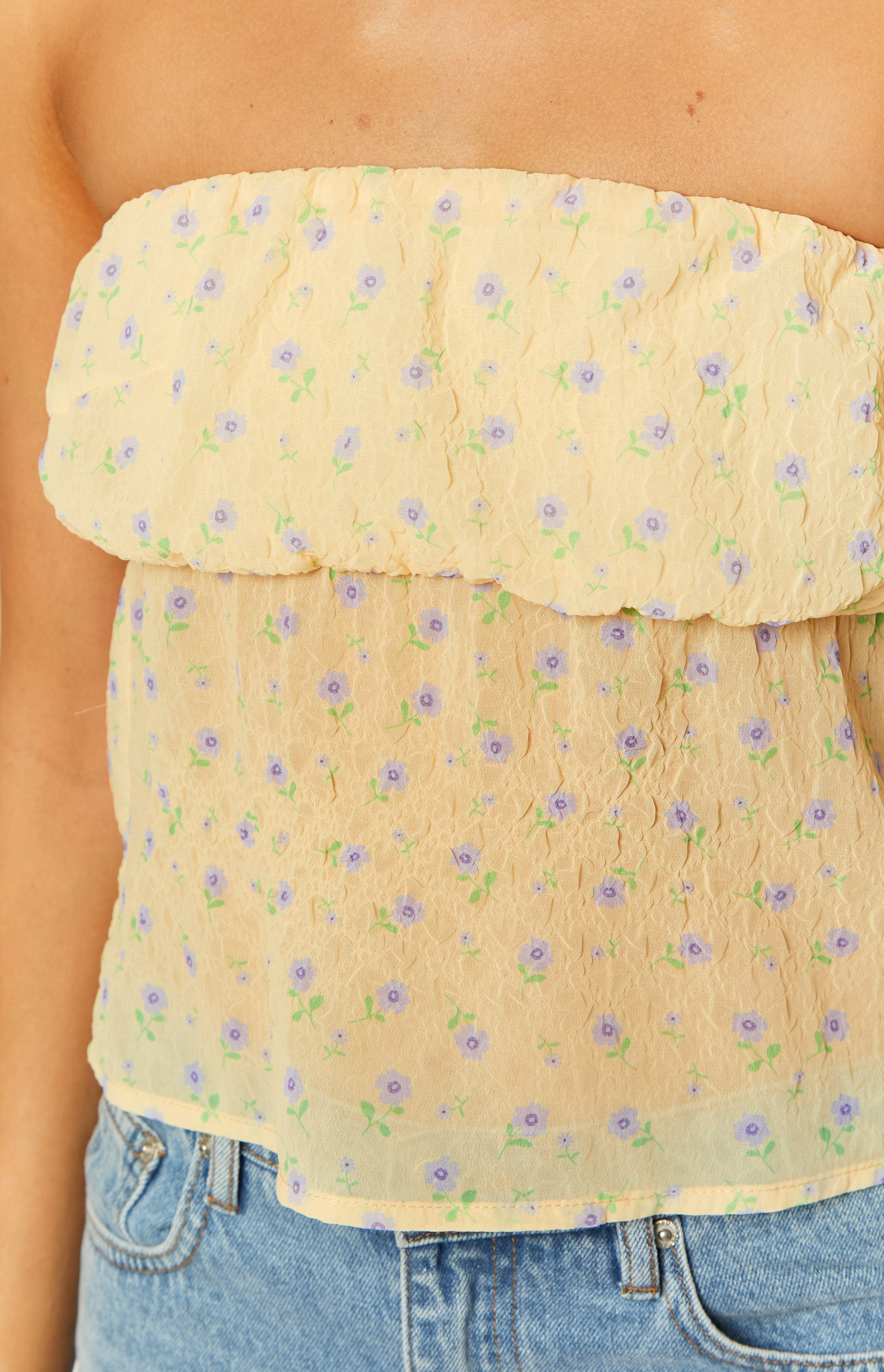 Close-up of the yellow crinkled strapless top showing its layered ruffle design and small purple floral print