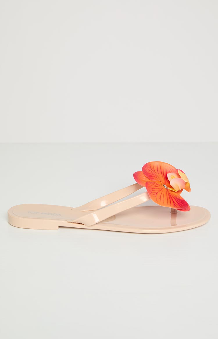 Side view of a tan thong sandal with a large orange and red floral embellishment on the strap