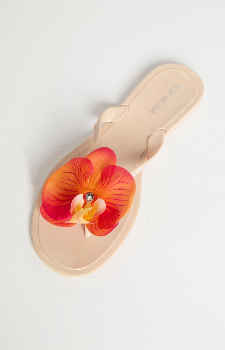 Overhead view of a tan thong sandal featuring a large orange, red, and yellow floral embellishment with a rhinestone center