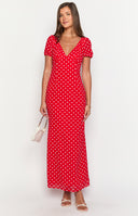 Brunette model wearing a red and white polka dot maxi dress with gold bracelets and holding a white hand bag.