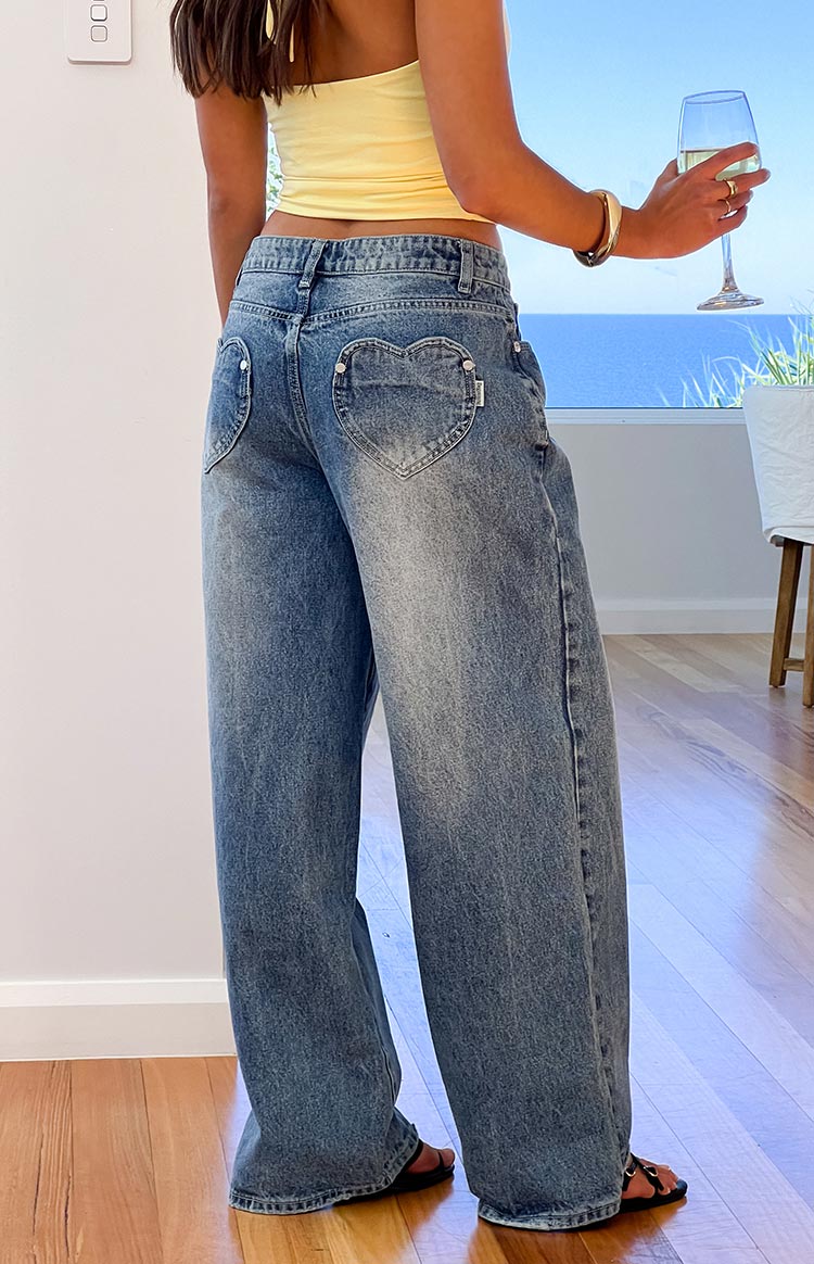 Back view of mid-wash denim slouchy jeans with unique heart-shaped back pockets and a relaxed wide leg fit
