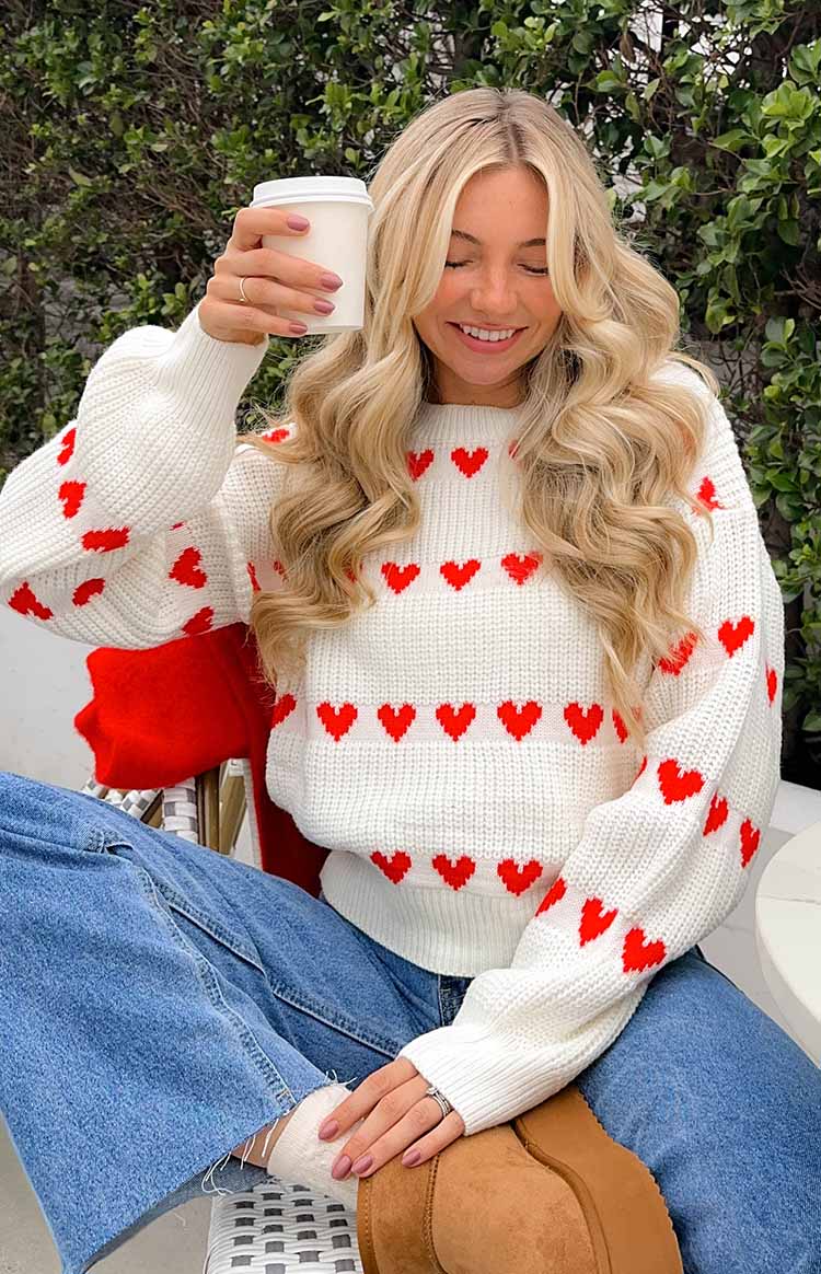 White knitted jumper with red heart patterns on the body and sleeves, featuring a crew neck and ribbed cuffs