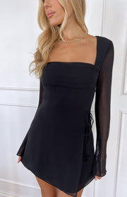Close-up of a black mini dress with a square neckline, sheer long sleeves, ruched bust, and side tie detail