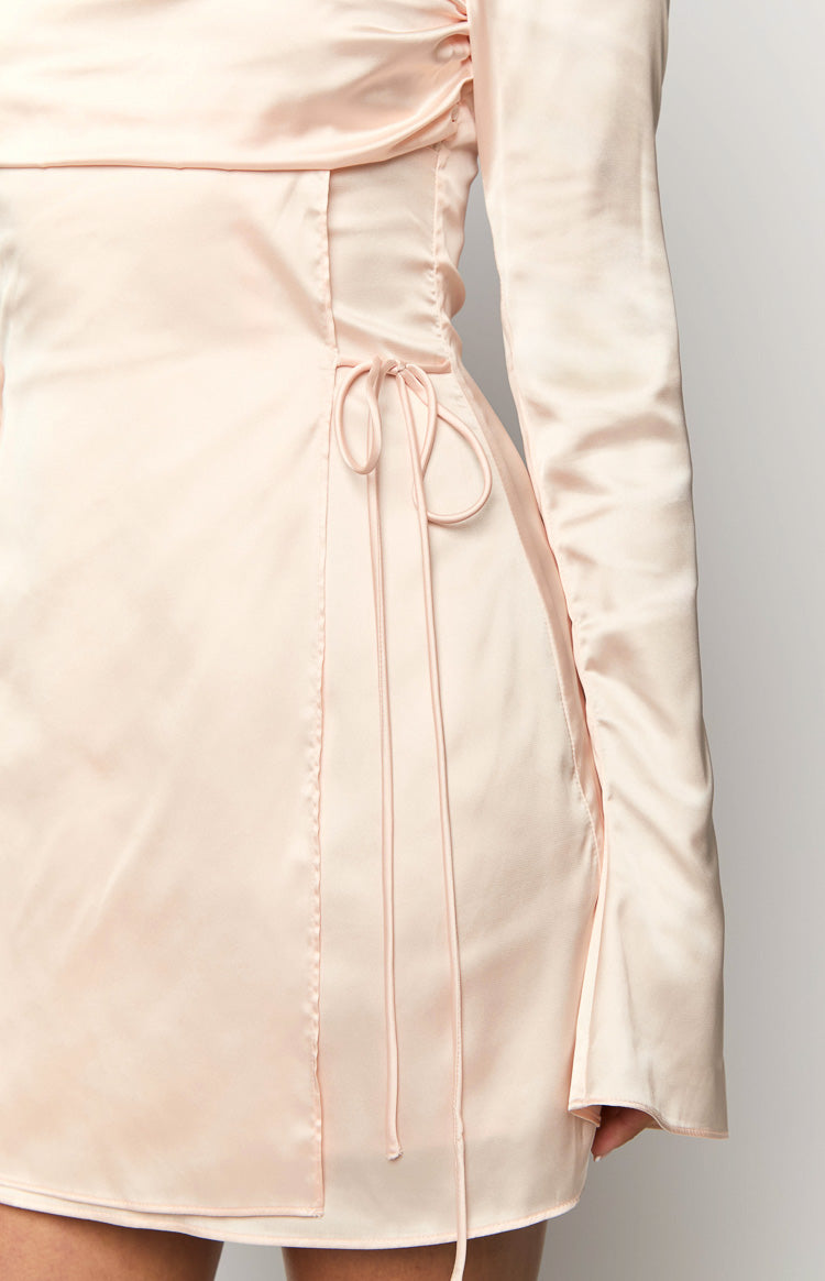 Close-up of the adjustable side ruching with delicate ties and long sleeve on a cream satin mini dress